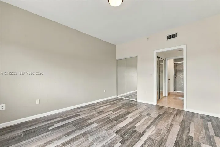 Neutral-toned interior featuring wood-finish flooring, high ceilings, and floor-to-ceiling mirrored closet doors