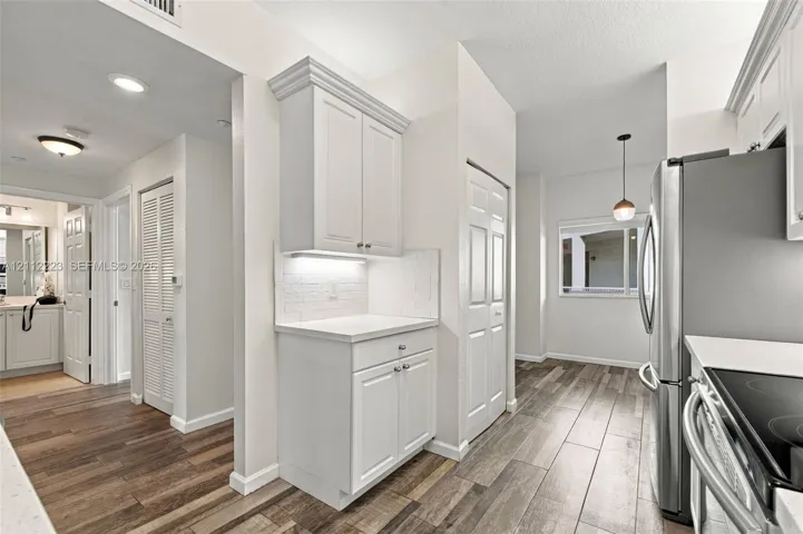 Kitchen featuring wood-finish flooring, white cabinetry with crown molding, stone-surface countertops, subway tile backsplash, and stainless steel appliances