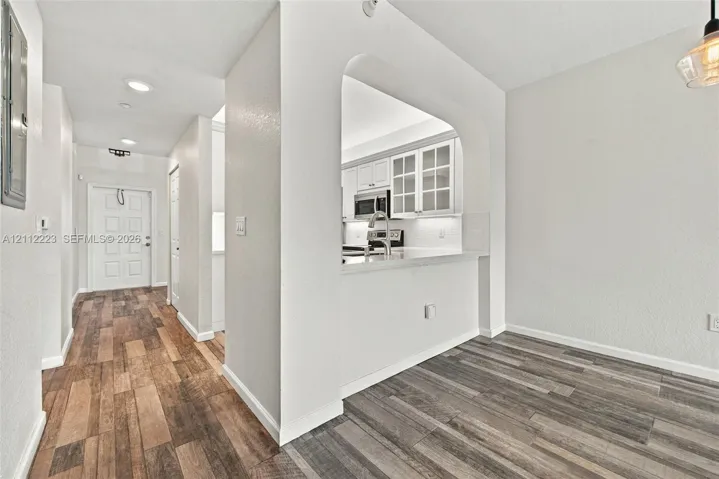 Arched pass-through window, wood-finish flooring, white cabinetry with glass-panel doors, recessed lighting, and stainless steel appliances
