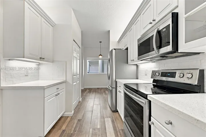 Kitchen featuring white shaker-style cabinetry, stainless steel appliances, white textured-brick backsplash, stone-surface countertops, and wood-finish flooring