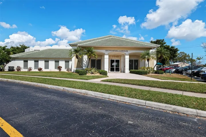 Clubhouse exterior featuring a hipped tile roof, arched entryway, stucco facade, and professional landscaping