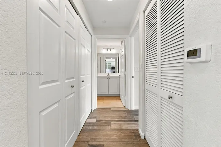 Hallway featuring wood-finish flooring, dual sets of bi-fold closet doors, louvered utility closet door, and wall-mounted digital thermostat
