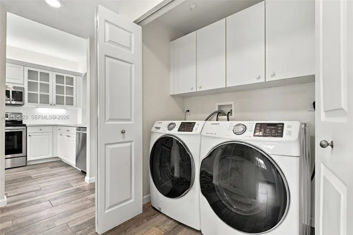 Laundry area featuring white built-in upper cabinetry and wood-finish flooring