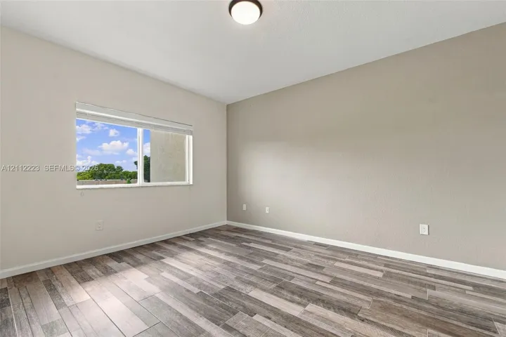 Interior space featuring wood-finish flooring, neutral wall tones, a flush-mount ceiling light, and a window with horizontal blinds