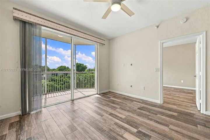 Wood-finish tile flooring, integrated ceiling fan, and sliding glass doors with direct access to a private covered balcony featuring metal railing