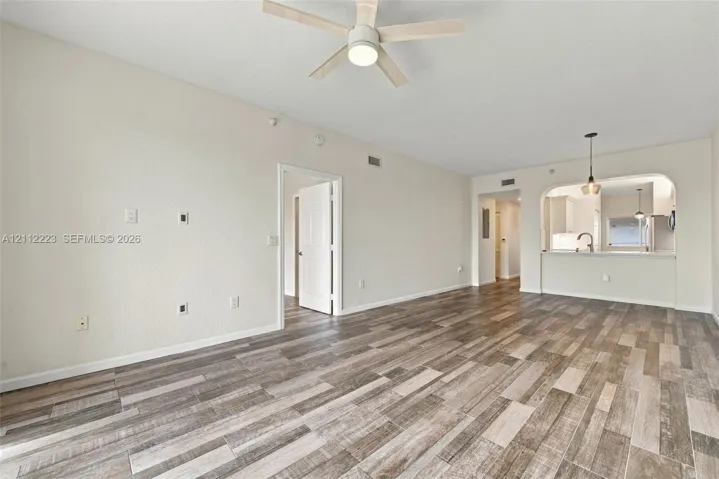 Open-concept space featuring wood-finish flooring, a ceiling fan, and a pass-through opening with a breakfast bar