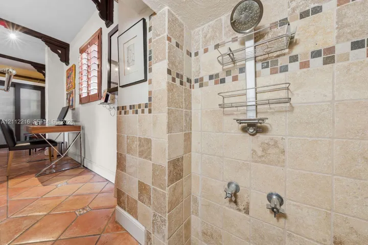 Shower stall featuring square-cut natural stone wall tile, decorative mosaic accent banding, a chrome-finish shower head, and dual-handle wall-mounted faucets