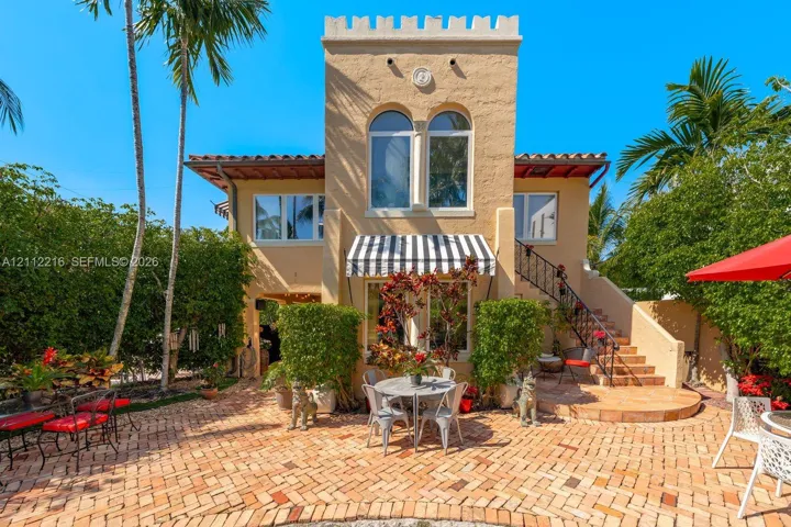 Mediterranean-style exterior featuring a crenellated tower, herringbone-pattern brick patio, arched windows, and an exterior wrought iron staircase