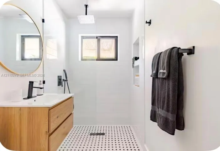 Bathroom featuring a floating wood-finish vanity, circular mirror, walk-in shower with matte black rainfall showerhead, and a built-in wall niche