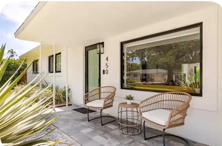 Mid-century modern exterior featuring white smooth-finish siding, large picture window with dark framing, covered entryway, and stone tile flooring