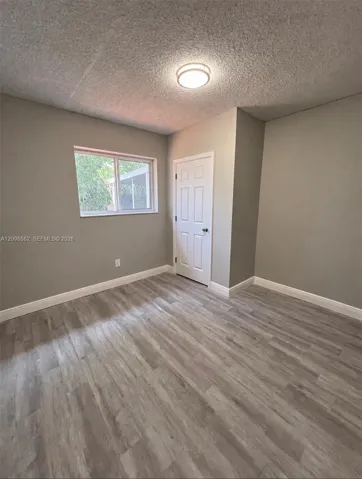 Room featuring wood-finish flooring, neutral wall paint, a six-panel door, and a flush-mount ceiling light fixture