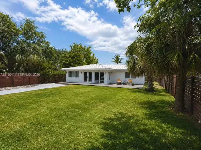 Single-story residence featuring a metal roof, white exterior, multi-panel glass doors, wood-slat fencing, and a spacious lawn