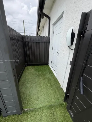 Stucco exterior wall featuring an electric vehicle charging station, synthetic turf surface, and dark-finished privacy fencing