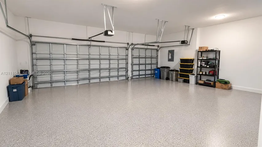 Three-car garage featuring a speckled epoxy floor coating, two paneled overhead doors, and dual garage door openers