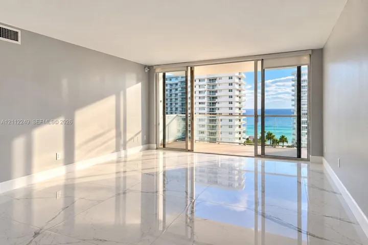 Floor-to-ceiling sliding glass doors, large-format polished tile flooring, and a glass-paneled balcony overlooking the ocean