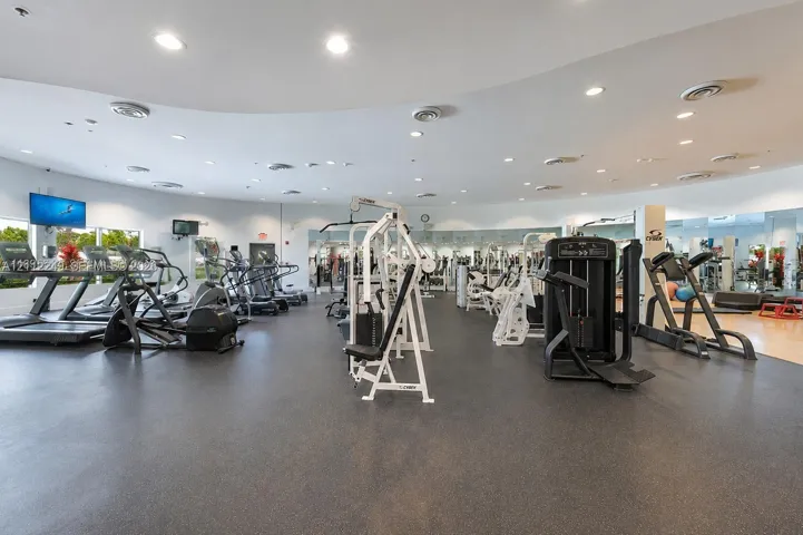 Fitness center featuring a curved ceiling design, recessed lighting, expansive wall-to-wall mirrors, rubberized flooring, and multiple built-in ventilation registers