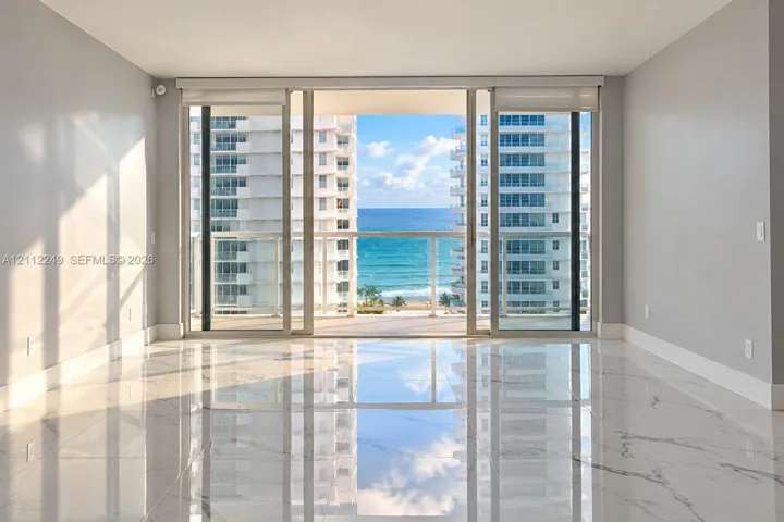 Polished stone flooring, floor-to-ceiling sliding glass doors, and a glass-paneled balcony overlooking the ocean