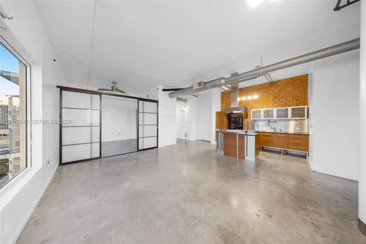 Open-concept interior featuring polished concrete flooring, exposed structural ductwork, industrial brick accent wall, and sliding frosted-glass privacy partition