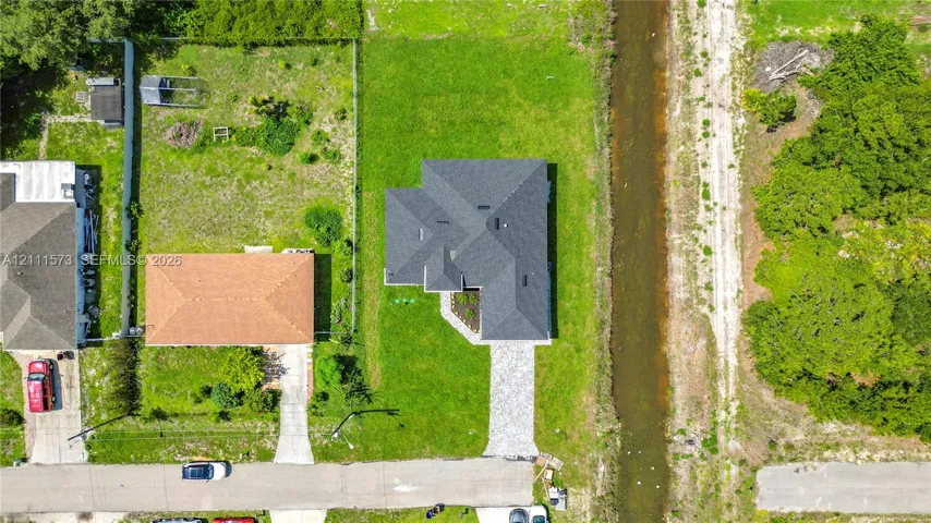 Aerial view featuring a multi-pitched asphalt shingle roof, paved concrete driveway, and expansive grass lot