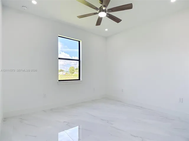 Neutral-toned interior space featuring white-finish tile flooring, recessed lighting, a ceiling fan with integrated lighting, and a single-pane window with a black frame