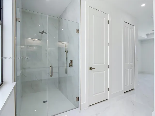 Walk-in shower featuring a frameless glass enclosure, floor-to-ceiling large-format tile surround, rainfall showerhead, handheld sprayer, and polished metallic fixtures