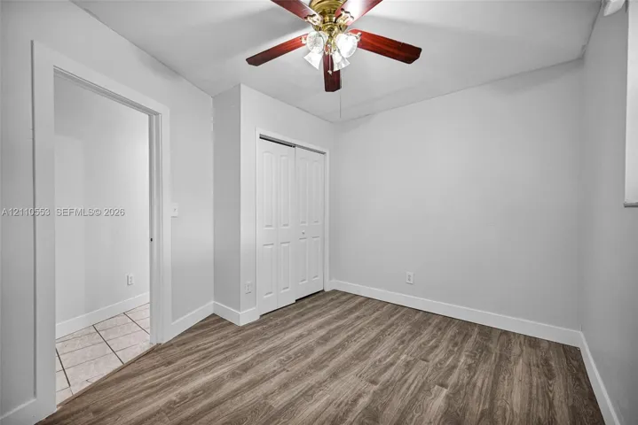 Room featuring wood-finish flooring, a ceiling fan with integrated lighting, and a dual-panel closet door