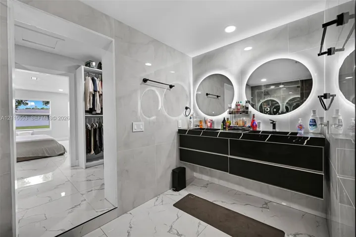 Floating black vanity featuring dual vessel sinks, quartz countertop, large circular backlit mirrors, and floor-to-ceiling large-format wall and floor tile