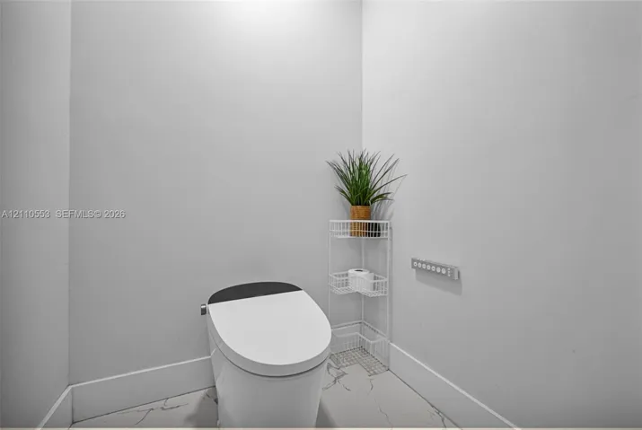 Modern one-piece smart toilet featuring a streamlined profile and contrast lid, set against large-format tile flooring with marble-finish veining and wall-mounted digital control panel