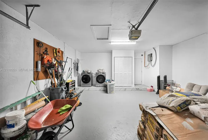 Attached garage featuring a concrete floor, built-in wall storage board, overhead fluorescent lighting, and an integrated laundry area with louvered closet doors