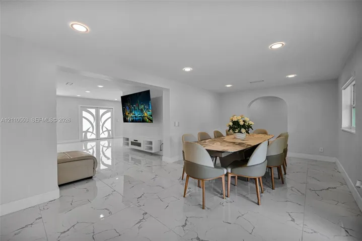 Polished stone-look flooring, recessed lighting, double entry doors with decorative glass inserts, and a distinct arched doorway