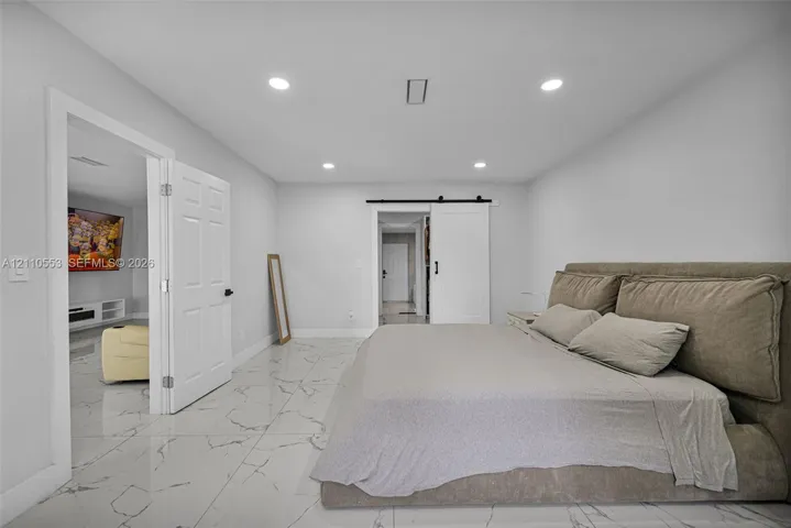 Polished tile flooring with veining, recessed lighting, white panel doors, and a sliding barn door with matte black hardware
