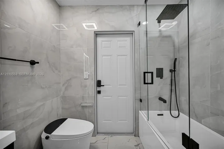 Full-height large-format wall tiling, glass-enclosed shower with a rainfall showerhead, matte black hardware, and integrated digital-flush toilet