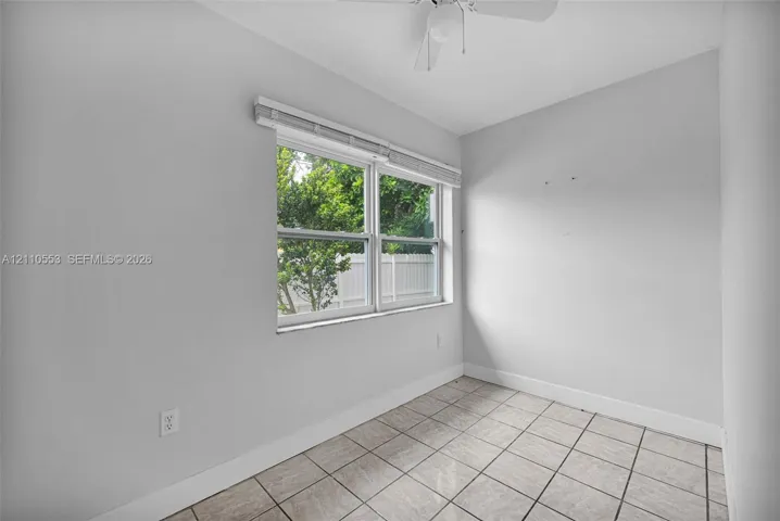 Neutral-toned room featuring tile flooring, a dual-pane window with white blinds, and a ceiling-mounted light fixture with a fan