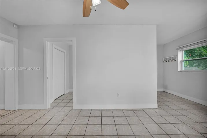 Neutral-toned interior space featuring large-format tile flooring, a ceiling fan with light fixture, and a wall-mounted hook rack