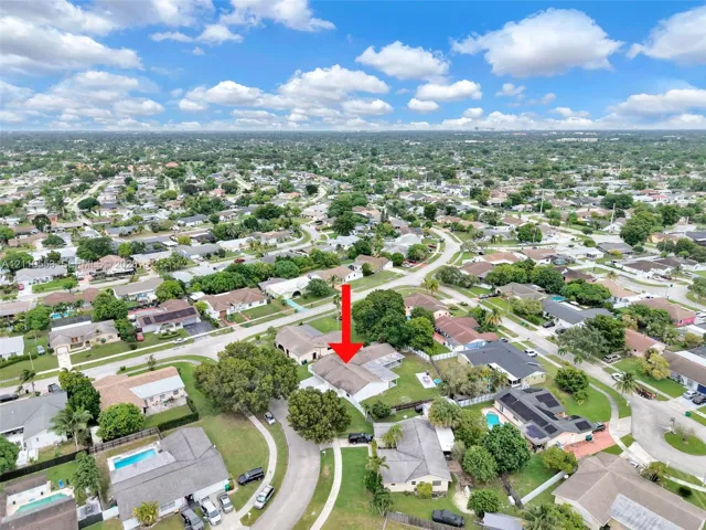 Aerial perspective featuring a single-story residence with a multi-gabled roofline and an attached garage, situated on a corner lot with mature landscaping