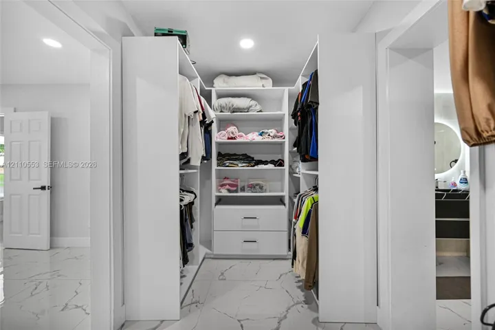 Walk-in closet featuring custom white built-in shelving, integrated dresser drawers, recessed lighting, and large-format tile flooring