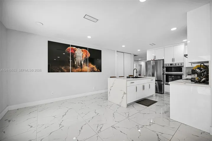 Kitchen featuring white high-gloss cabinetry, center island with stone-finish waterfall countertop, stainless steel double wall oven, and large-format porcelain tile flooring