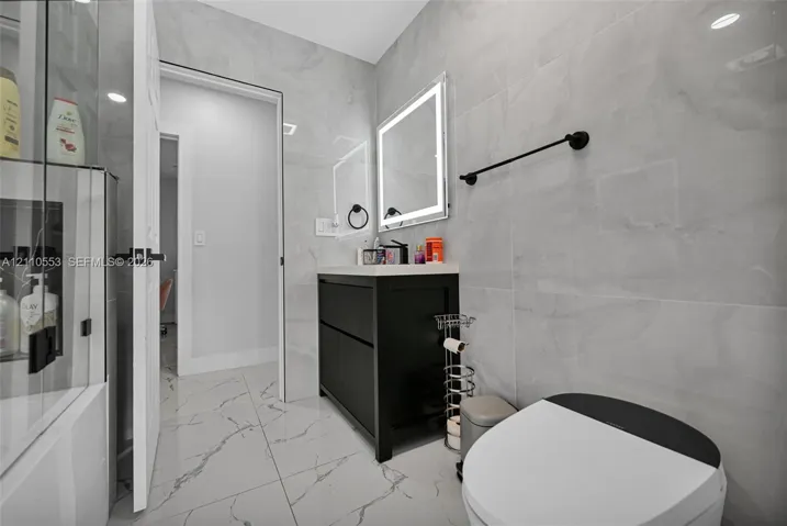 Bathroom featuring large-format porcelain tile wall cladding, a black floating vanity with a solid surface countertop, an LED-backlit mirror, and matte black hardware