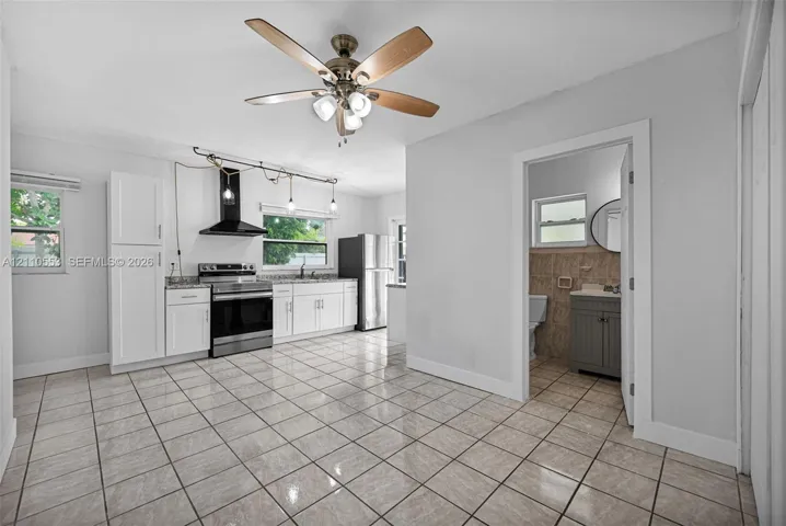 Kitchen featuring white cabinetry, stainless steel appliances, a black range hood, tile flooring, and a ceiling fan with integrated lighting