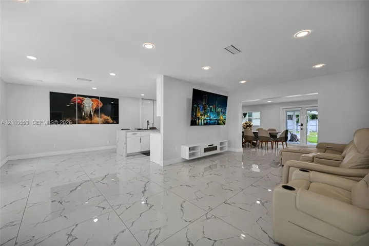 Large-format tile flooring with a neutral-veined pattern, recessed ceiling lighting, kitchen island with cabinetry, and double glass-paneled exterior doors