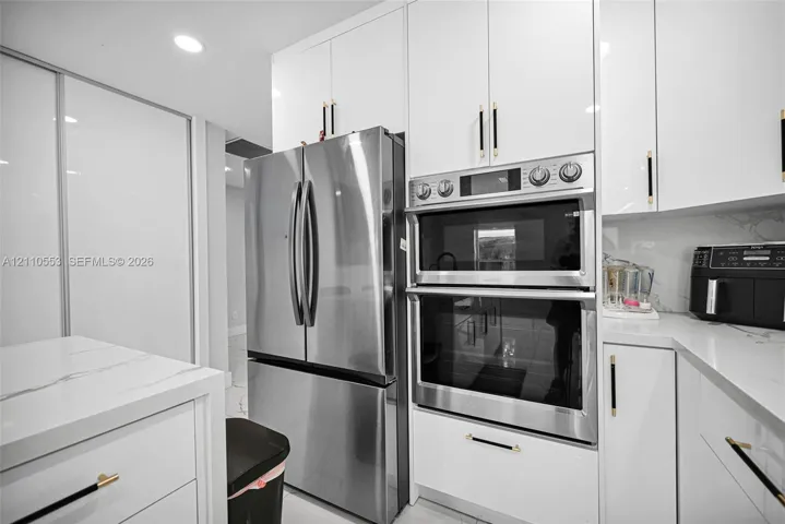 Kitchen featuring high-gloss white cabinetry, stone-finish countertops, stainless steel appliances, a double wall oven, and metallic hardware