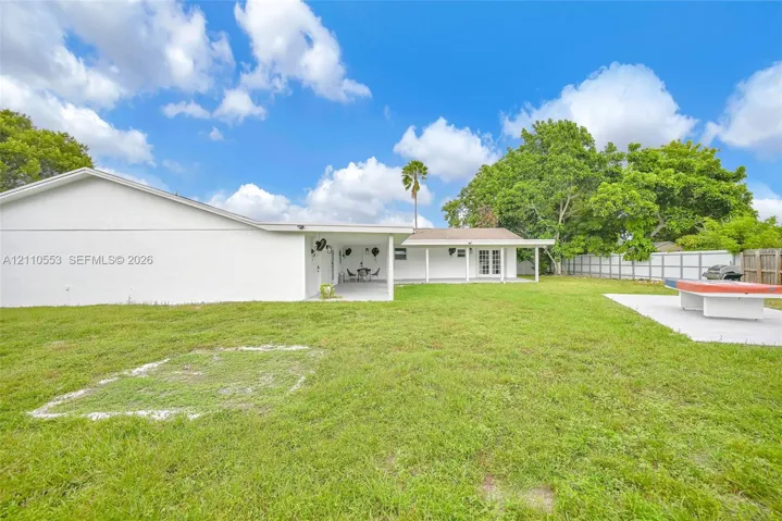 Backyard featuring a sprawling lawn, a covered patio area, concrete hardscaping, and perimeter wood and metal fencing