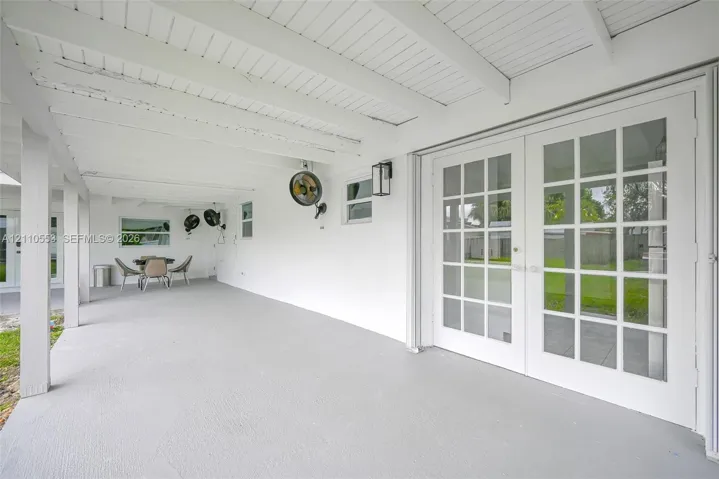 Covered patio featuring a painted wood-beam ceiling, glass-paned French doors, exterior wall-mounted lighting, and concrete flooring