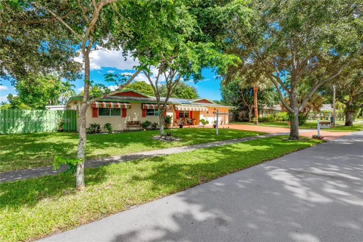 Single-story residence featuring a low-pitch roofline, integrated window awnings, a paved driveway, and mature landscaping within a grassy front yard