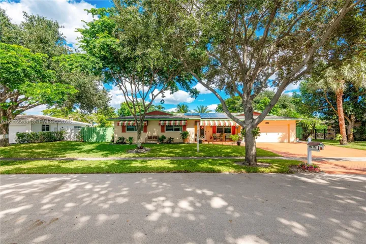 Single-story residence featuring a paved driveway, attached garage, solar panels, and mature landscaping