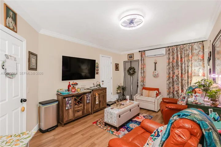 Living area featuring crown molding, wood-finish flooring, a wall-mounted ductless air conditioning unit, and a flush-mount circular LED ceiling light fixture