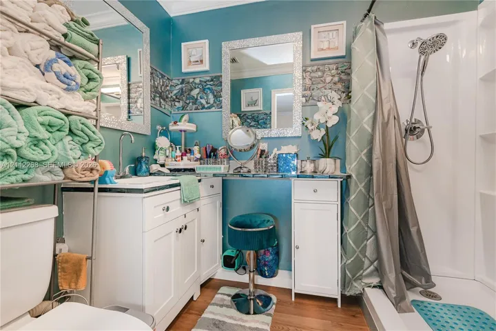 White vanity with integrated storage, decorative stone-tile backsplash, wall-mounted mirror with mosaic-style frame, and shower unit with handheld fixture