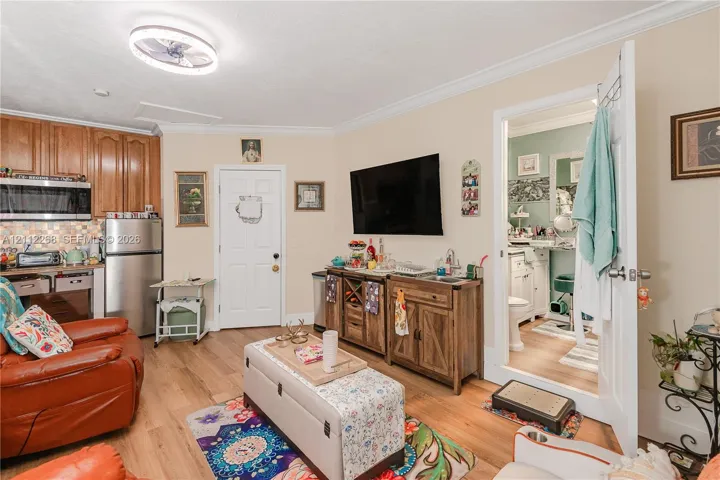 Kitchenette featuring wood-finish cabinetry, stainless steel microwave, and integrated tiled backsplash, complemented by wood-finish flooring and crown molding