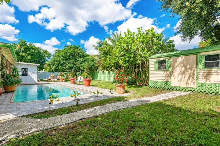 Backyard featuring a concrete-paver patio, swimming pool, detached storage structure, manicured lawn, and perimeter lattice fencing