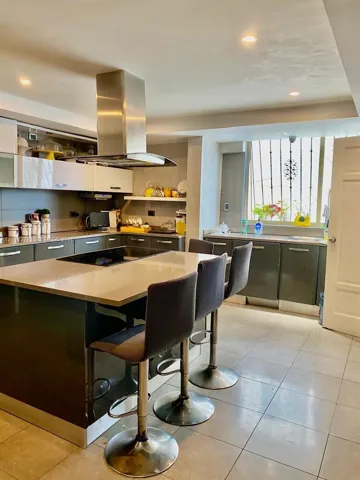 Kitchen featuring an island with a stone-surface countertop, high-gloss cabinetry, stainless steel range hood, recessed ceiling lighting, and large-format tile flooring